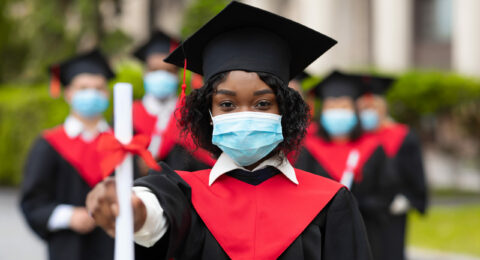 African american young lady in graduation costume and face mask