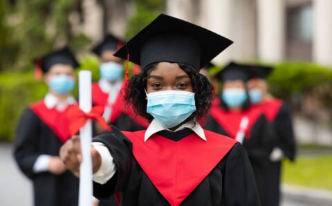 African american young lady in graduation costume and face mask